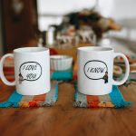 Two mugs with playful text on a table showcasing a cozy indoor setting.