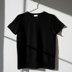 Home Minimalist image of a black t-shirt on a hanger with dramatic shadows on a white wall.